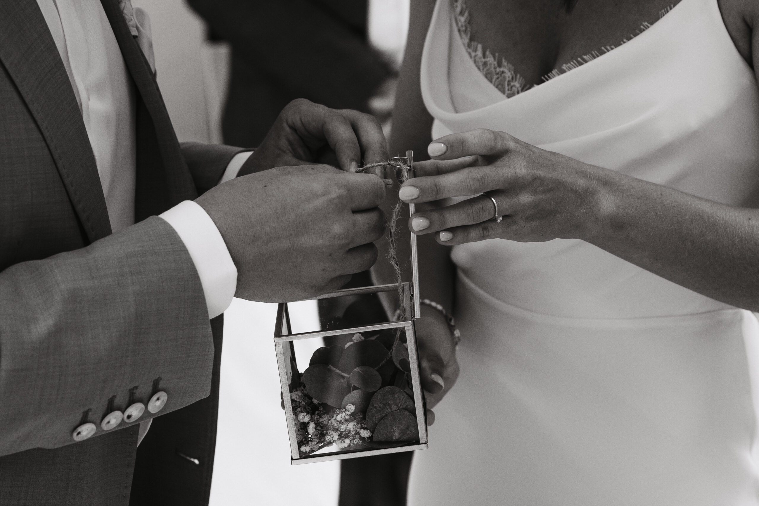 Das Brautpaar holt gemeinsam die Ringe aus der dekorativen Ringbox. Bild in Schwarz Weiß.