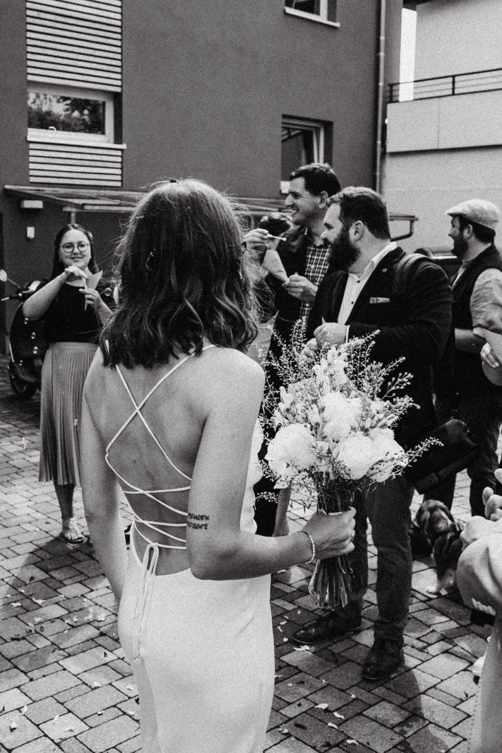 Die Braut schaut nach dem Standesamt zu ihren Gästen mit dem Rücken zur Kamera und dem Brautstrauss in der Hand. Bild in Schwarz weiß