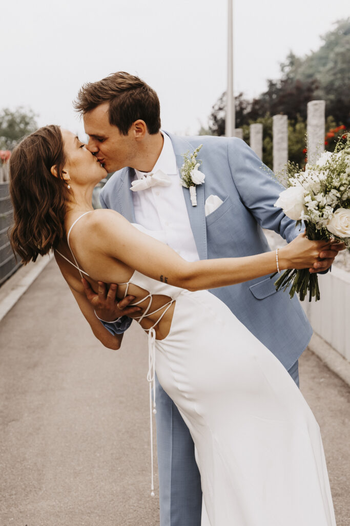 Der Bräutigam küsst seine Braut während der Aufnahme der Hochzeitsbilder und hält sie dabei im Arm.