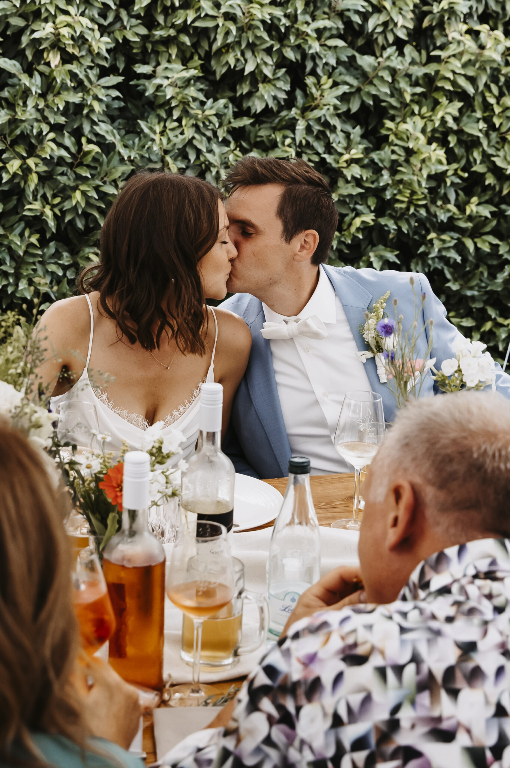 Brautpaar küsst sich an der Hochzeitstafel vor dem Essen und der anstehenden Gartenparty
