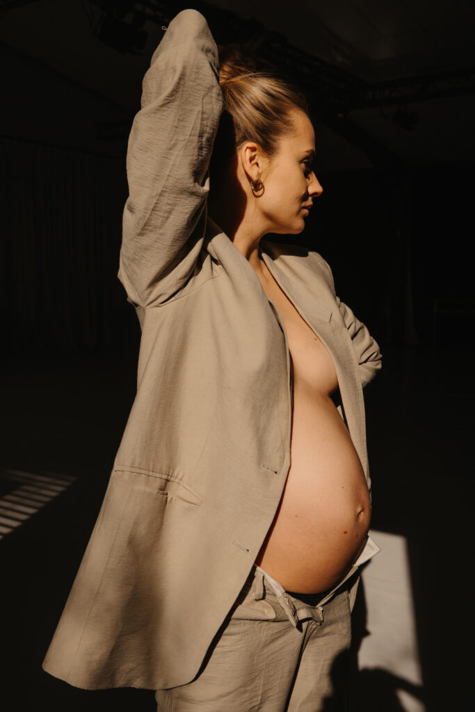 Eine schwangere Frau während dem Schwangerschaftsshooting. Ihr Babybauch wird von der Sonne angestrahlt.