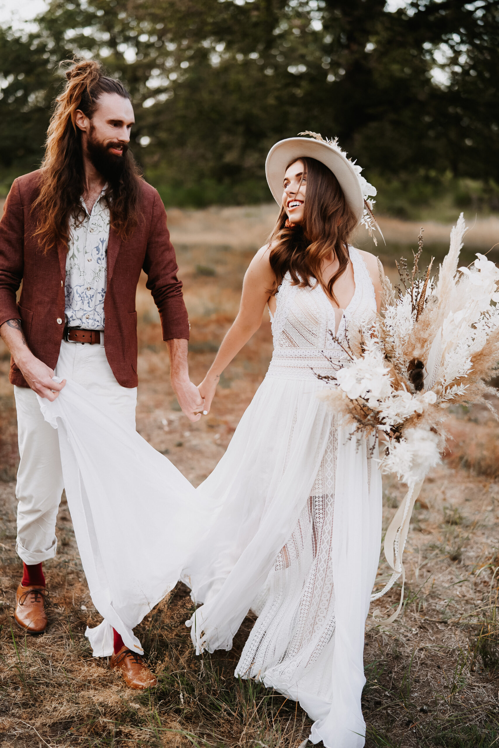 married BOHO Couple is walking together hand in hand on a field