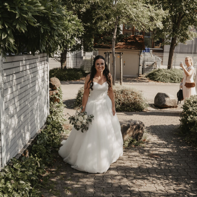 Die Braut läuft auf ihren Bräutigam zu Auf einem kleinem weg zum First Look und sie schaut dabei ganz gespannt.