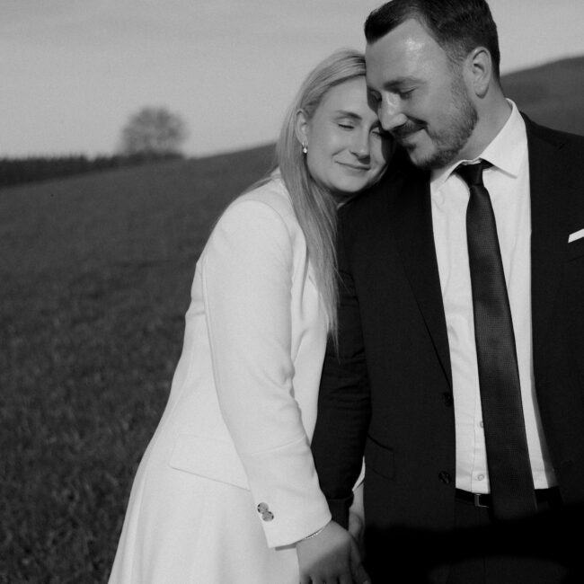 Brautpaarfoto mit Gesichtern, Paar kuschelt gemeinsam, Bild in schwarz weiß auf einer Wiese nach einer standesamtlichen Hochzeit