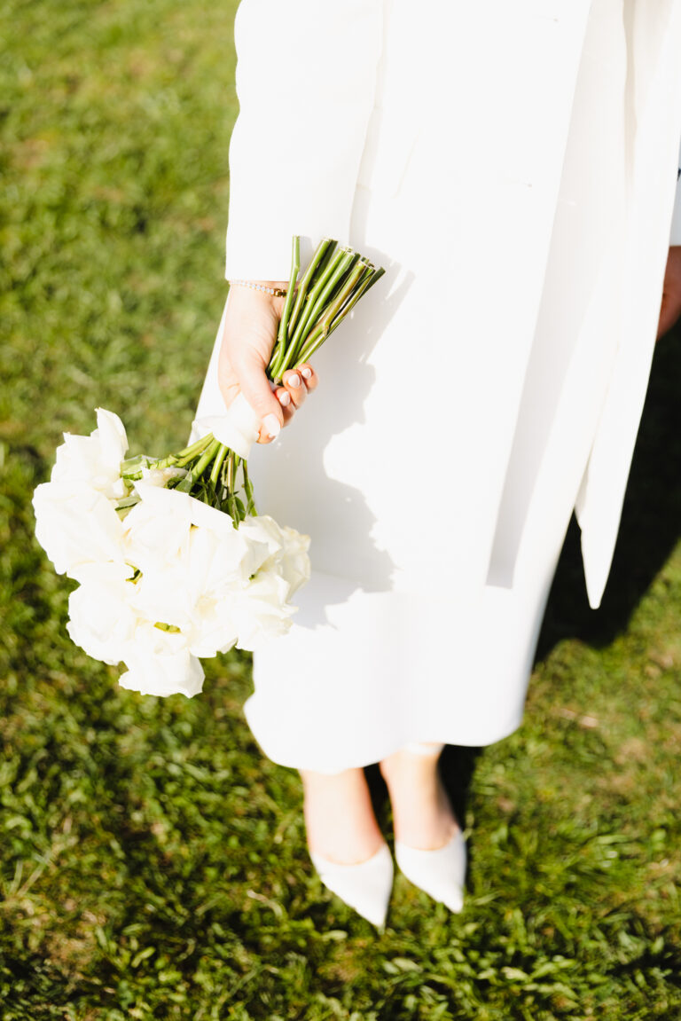 Brautoutfit - Kleid mit Blazer und High Heels. Alles in weiß mit dem Brautstrauss in der Hand. Bild aufgenommen auf der Halde in oberried während eines Brautpaarshootings