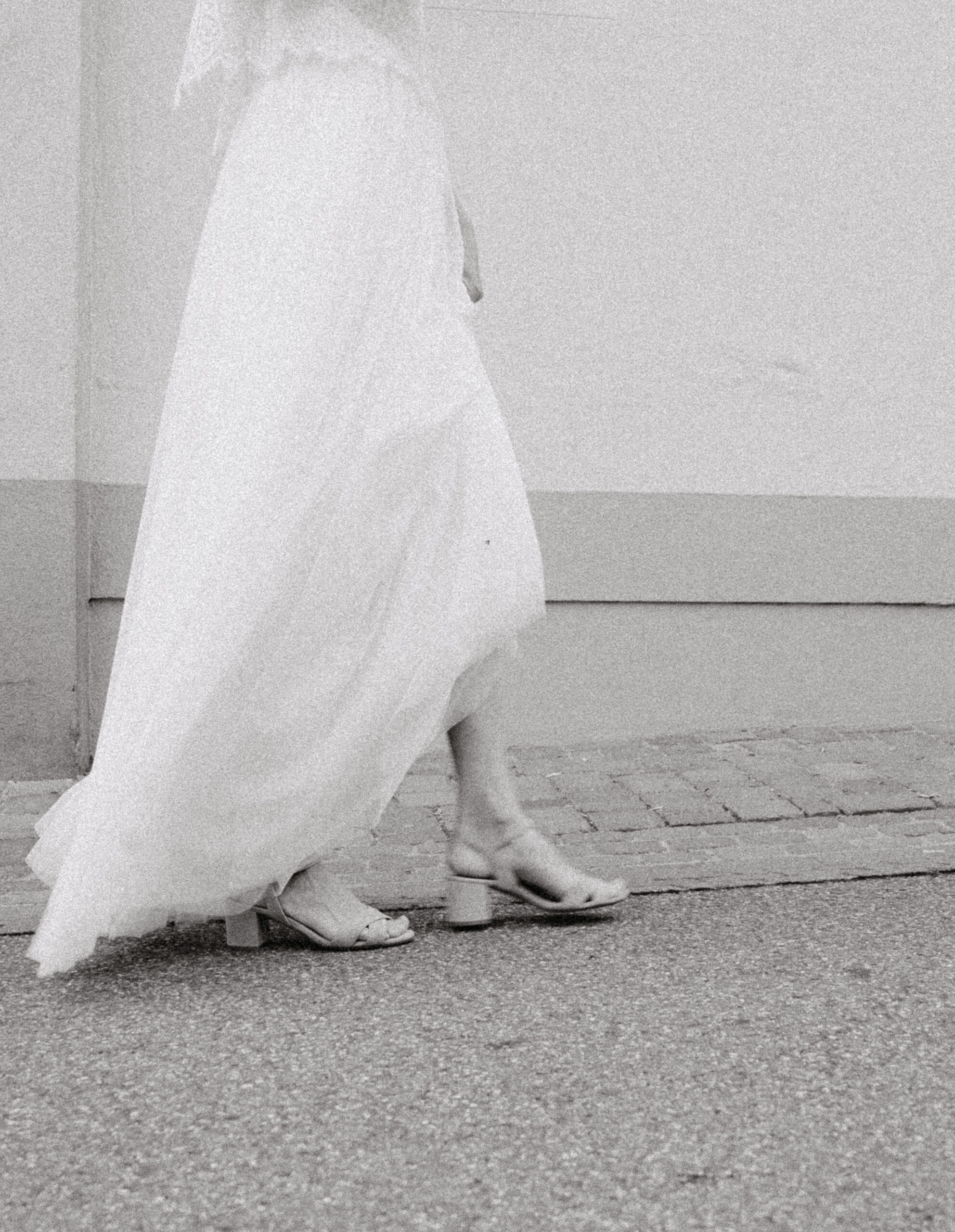 Detailaufnahme des Rocks und der offenen Brautschuhe der Braut während dem laufen. Bild in Schwarz Weiß.