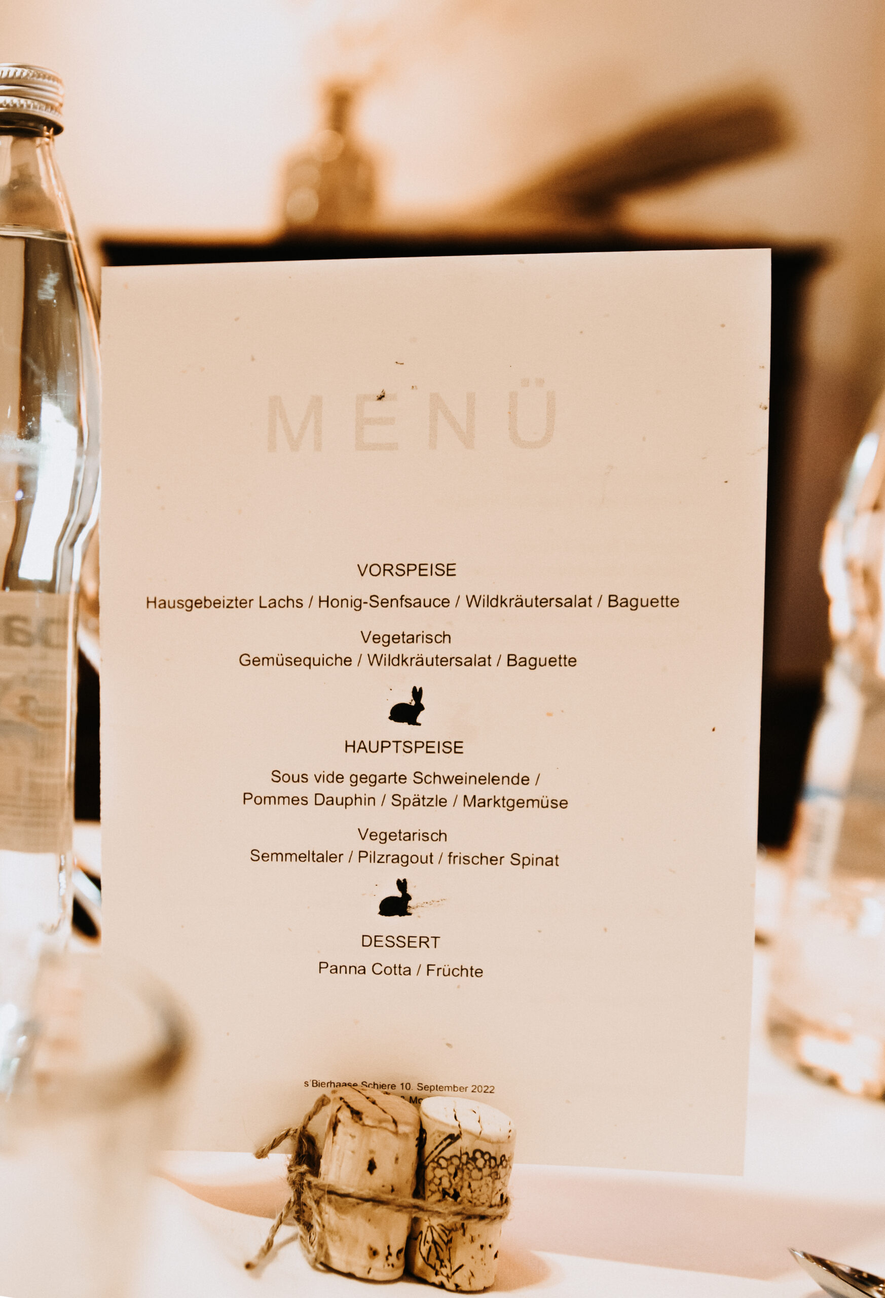 Detailaufnahme des Abend Menüs für die Hochzeitsgäste. Aufgeteilt in Vorspeise, Hauptspeise und Dessert. Das Menü ist eingeklemmt in Flaschenkorken.