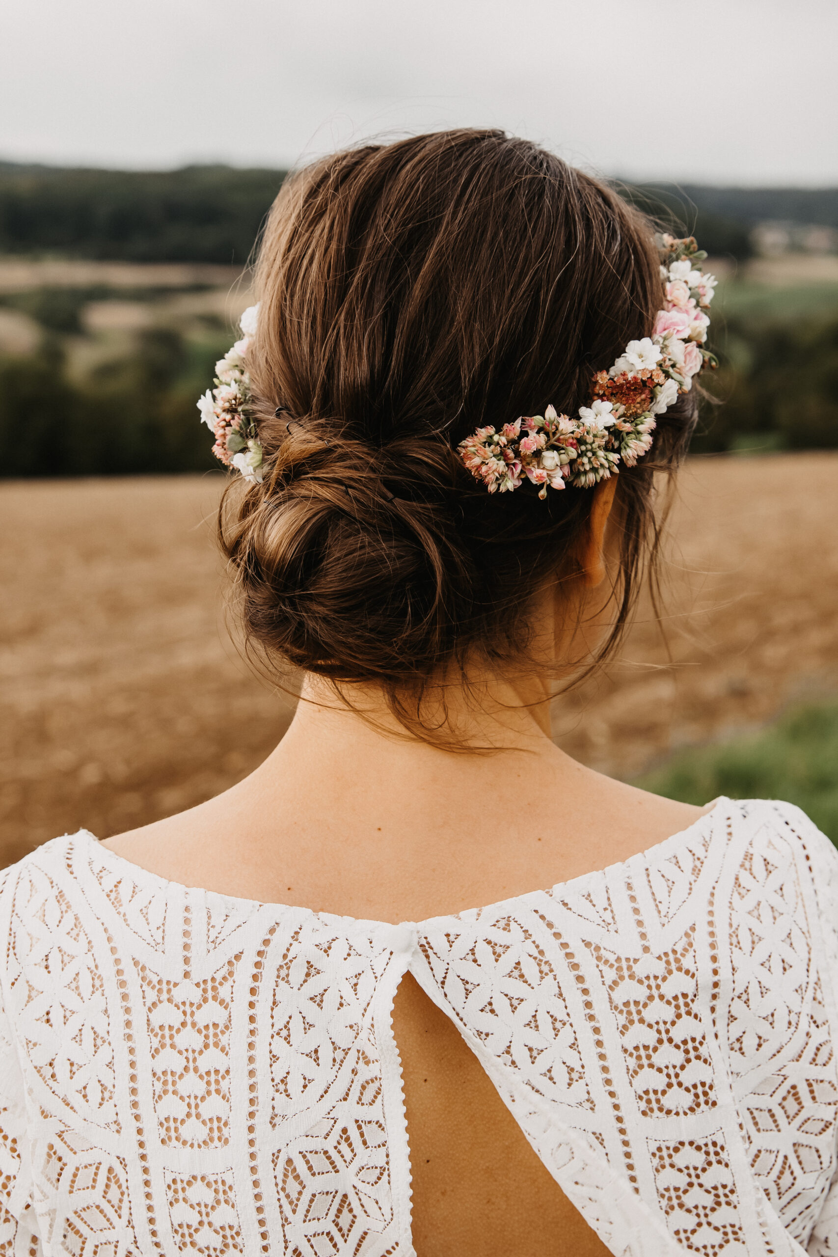 Braut von hinten mit Ihrer wunderschönen Brautfrisur bzw. Haarfrisur für Ihre Hochzeit und sie hat sich noch einen Blumenkranz für ihre Haare knüpfen lassen, sodass sie einen Blumenhaarkranz trägt in weiß und rosé.
