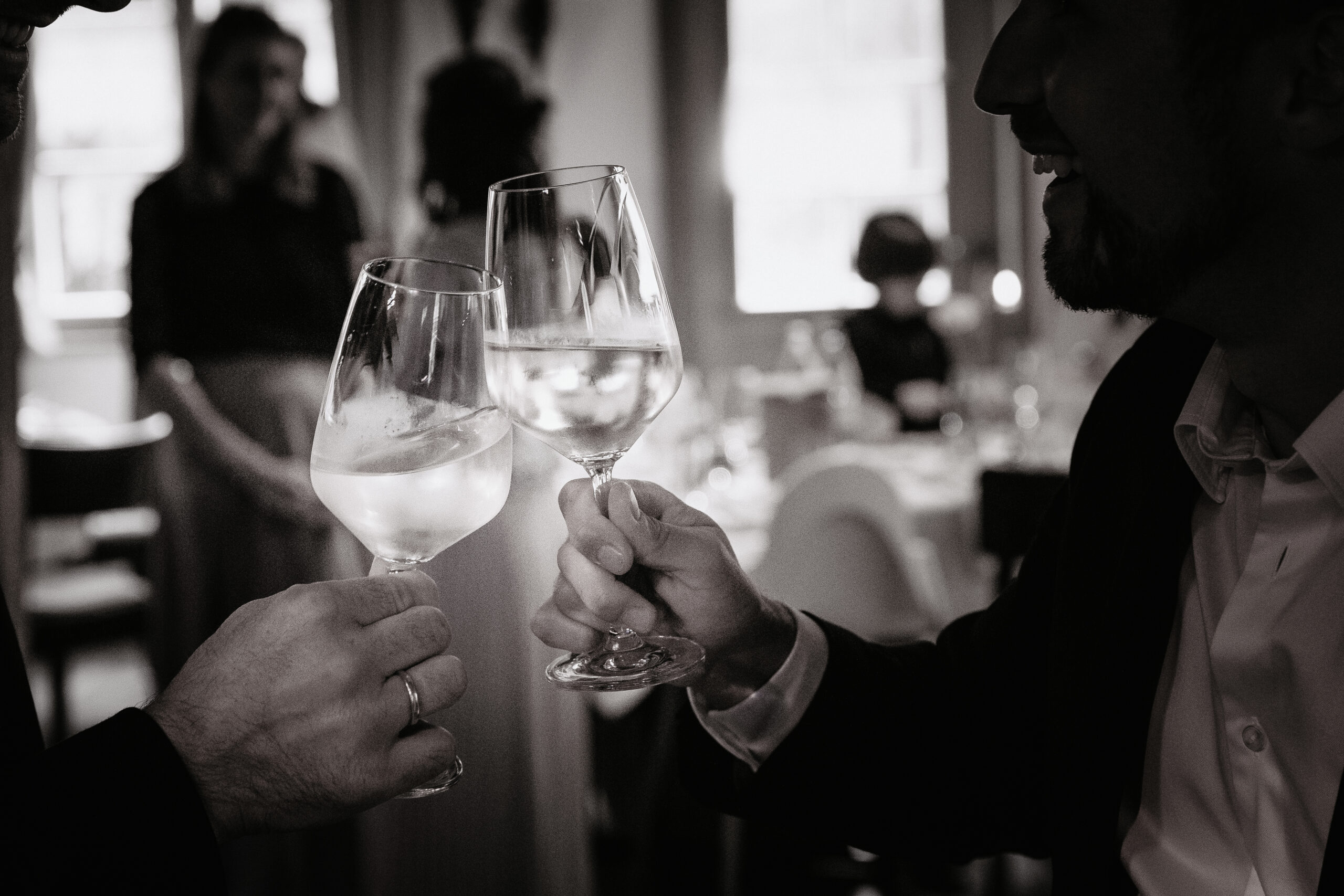 Hochzeitsgäste stoßen mit Rotwein auf das Brautpaar an. Bild in Schwarz weiß aufgenommen. Hochzeitsgesellschaft hat in Freiamt in der S‘ Bierhaase Schiere gefeiert.