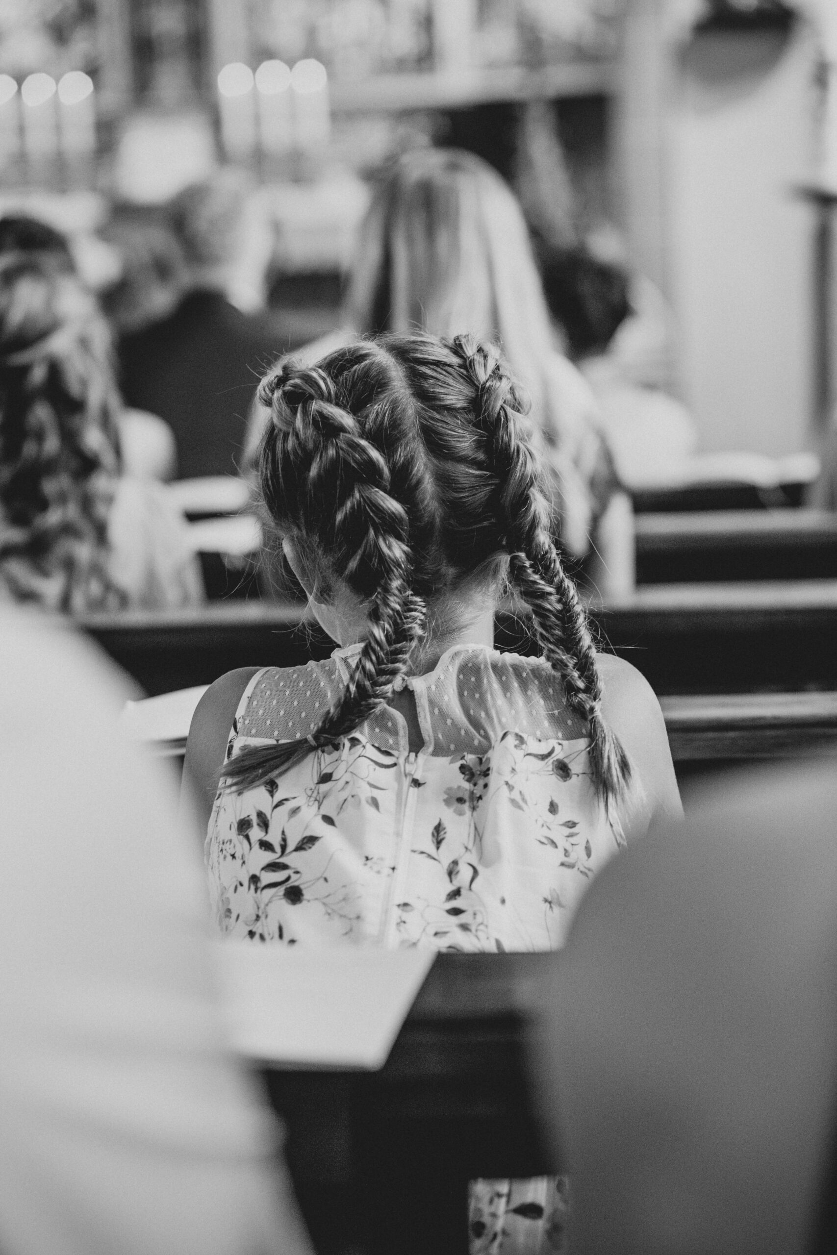 Detailaufnahme von hinten von einem kleinen Mädchen mit geflochtenen Zöpfen sie der kirchlichen Trauung zuschaut.