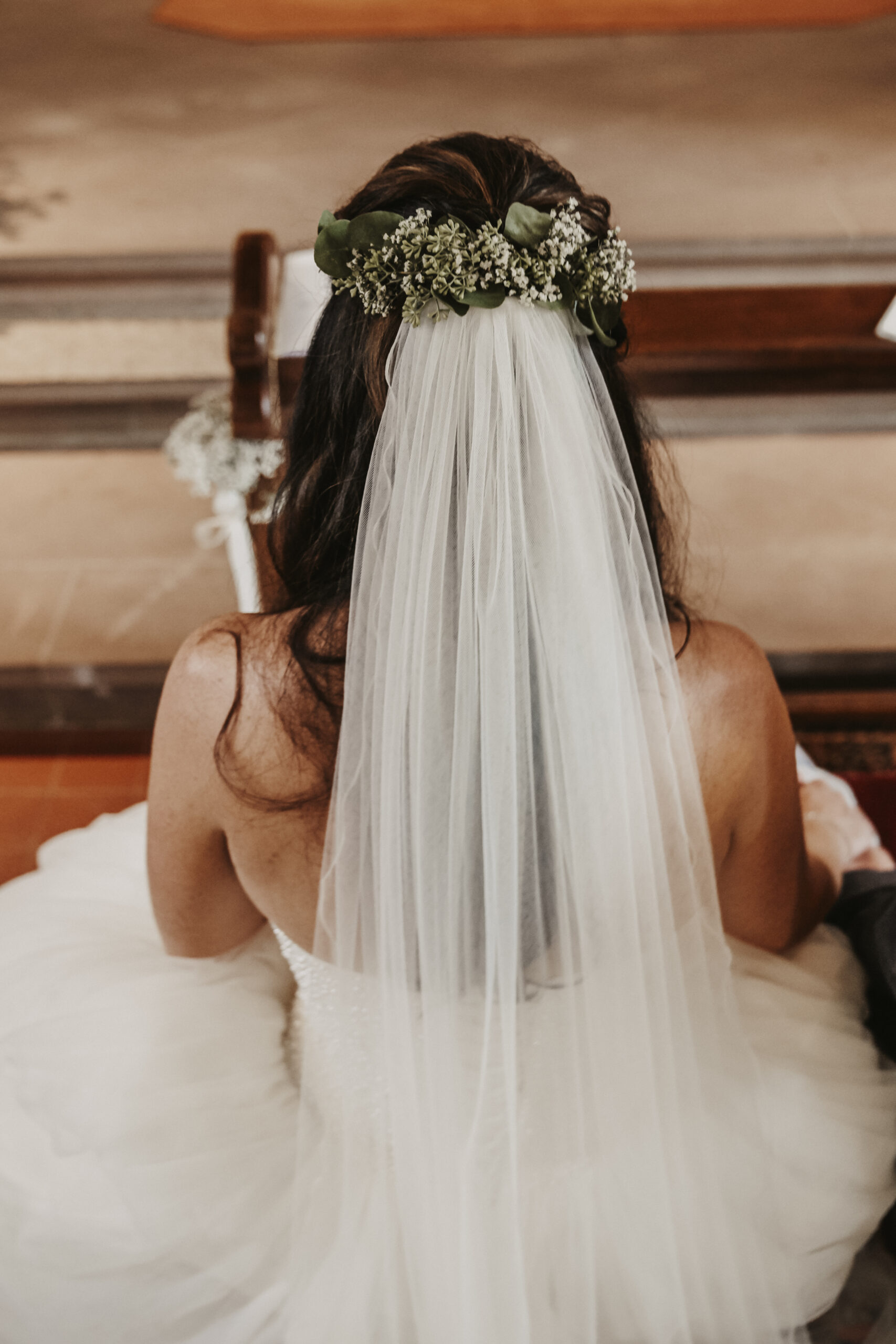 Braut von hinten oben mit großem Brautkleid und Schleier und der Schleier ist in den offenen Haaren mit Blumen festgesteckt als Hochzeitsfrisur.