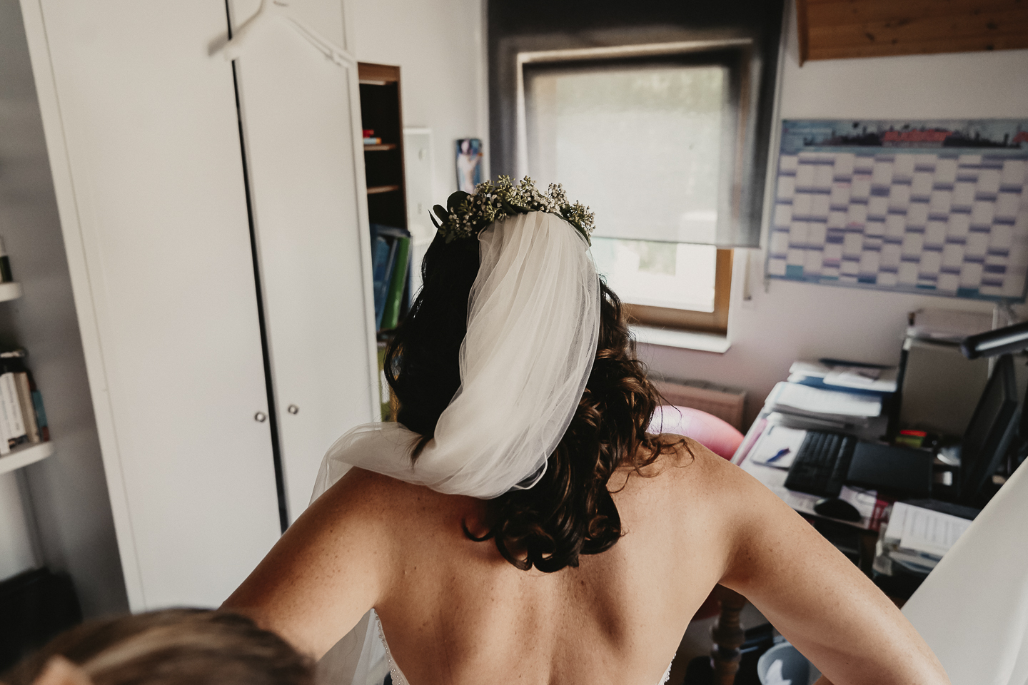 Die Braut mit fertigem Haar und Schleier beim Getting Ready zu Hause und beim Anziehen vom Kleid.