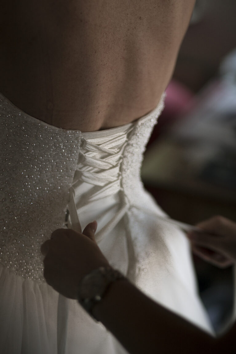 Die Trauzeugin hilft der Braut beim Anziehen und schnürt ihr das Kleid am Rücken zu.