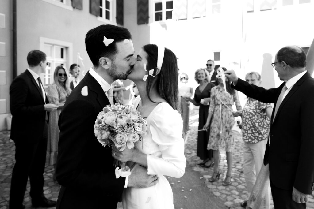 Der Hochzeitsfotograf hat ein frisch vermähltes Ehepaar vor dem Standesamt aufgenommen während dem die Hochzeitsgäste Spalier standen und Rosen geworfen haben.
