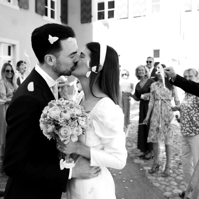 Der Hochzeitsfotograf hat ein frisch vermähltes Ehepaar vor dem Standesamt aufgenommen während dem die Hochzeitsgäste Spalier standen und Rosen geworfen haben.
