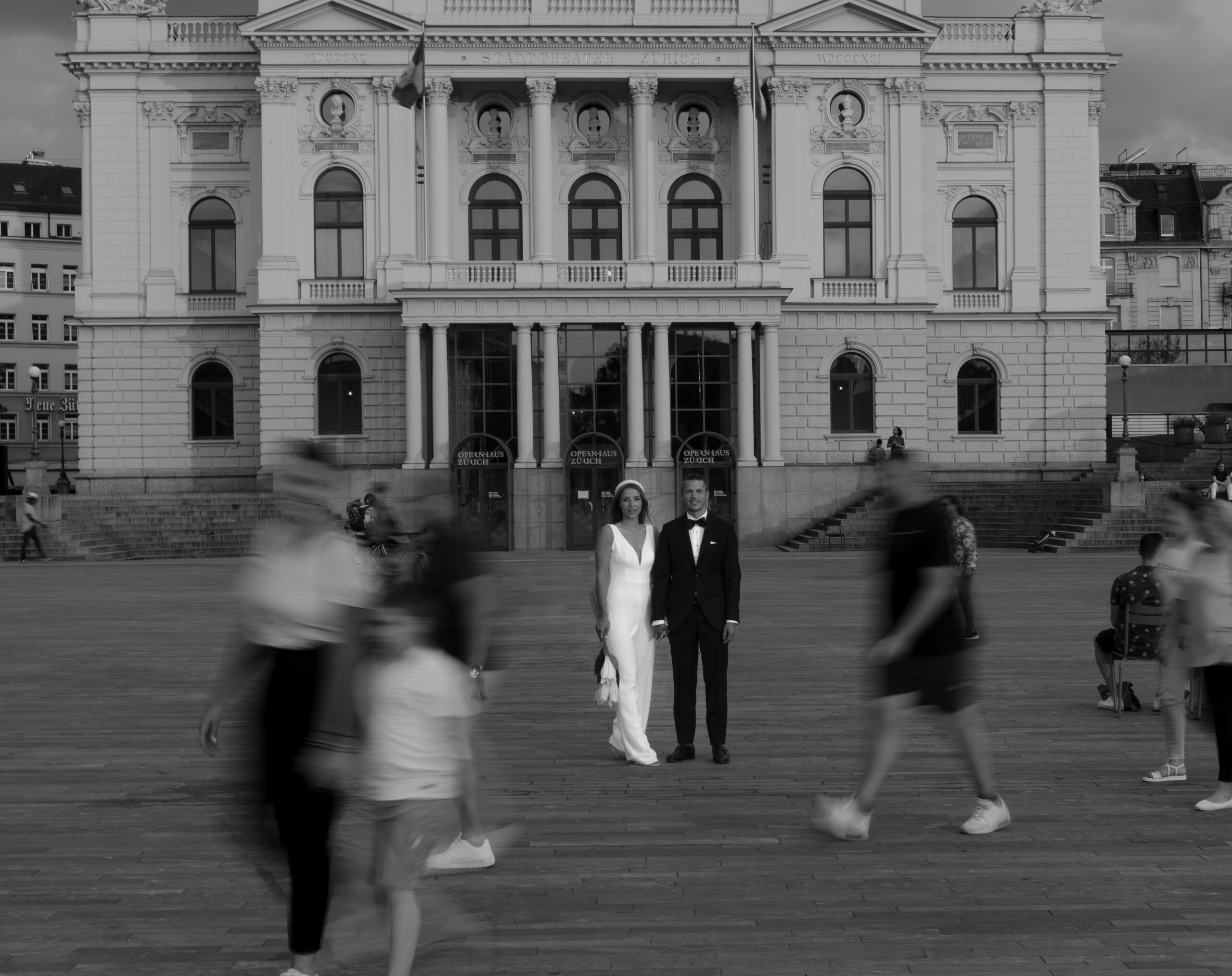 Das Brautpaar auf dem Bellevue Platz in Zürich während die anderen Personen vorbei laufen und verschwommen sind.