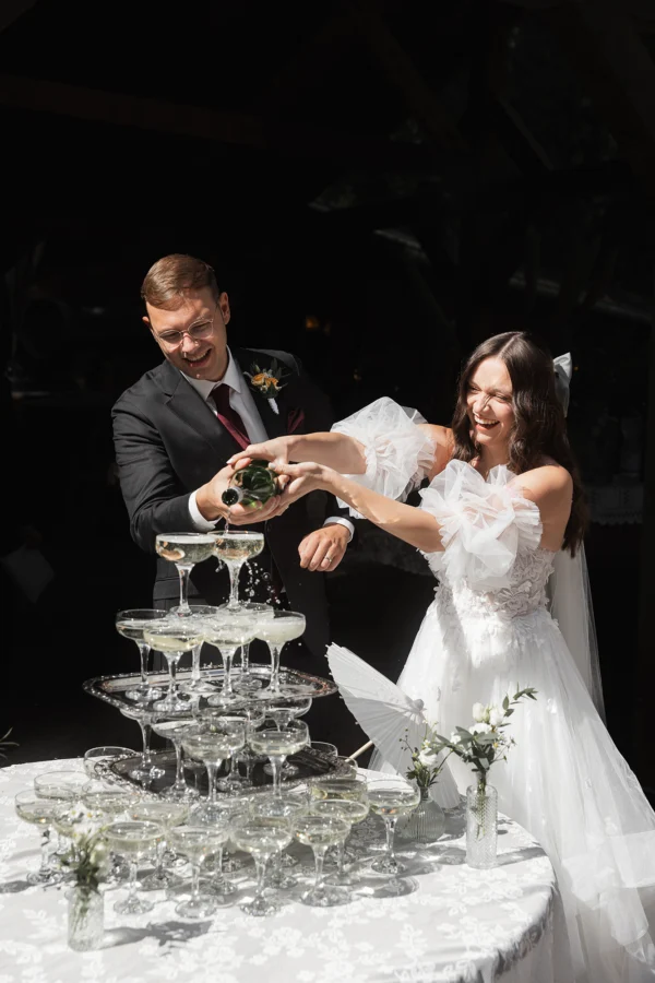 Das Hochzeitspaar füllt die Sekttorte und hat Spaß dabei. Danach trinken sie beide.